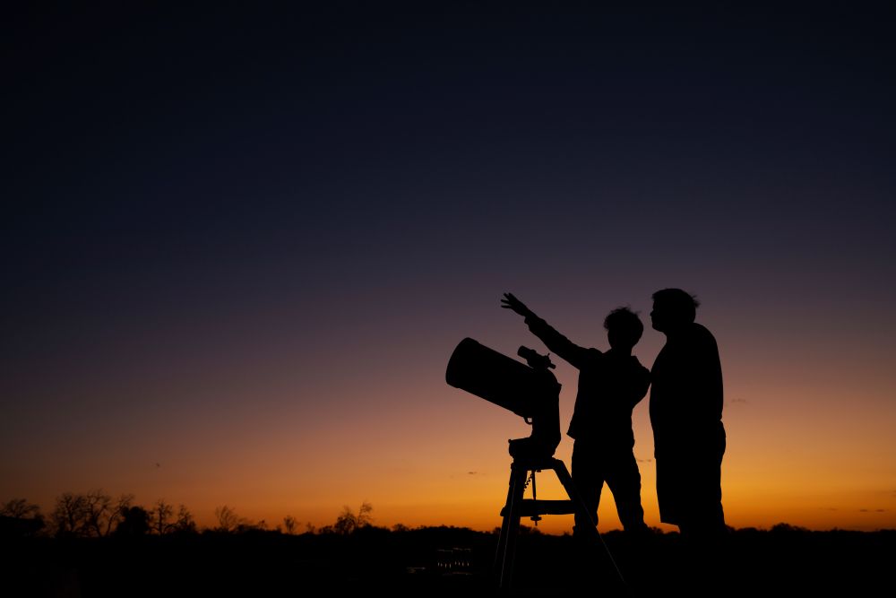 Two people using telescope with sunset in background
