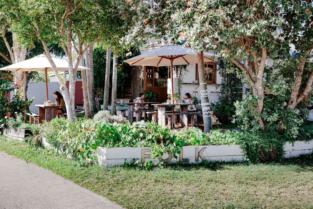 Outdoor dining at Folk Cafe with tables and umbrellas surrounded by a lush green yard.