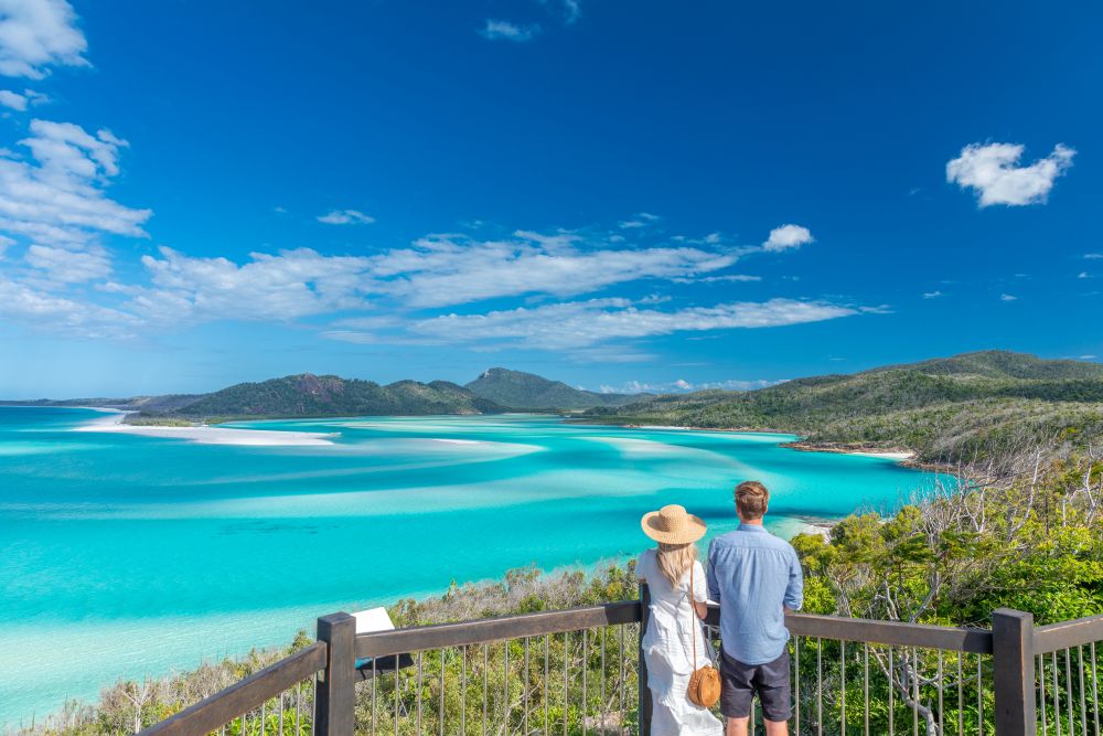 Two people at viewing platform looking at Whitehaven beach coastline.