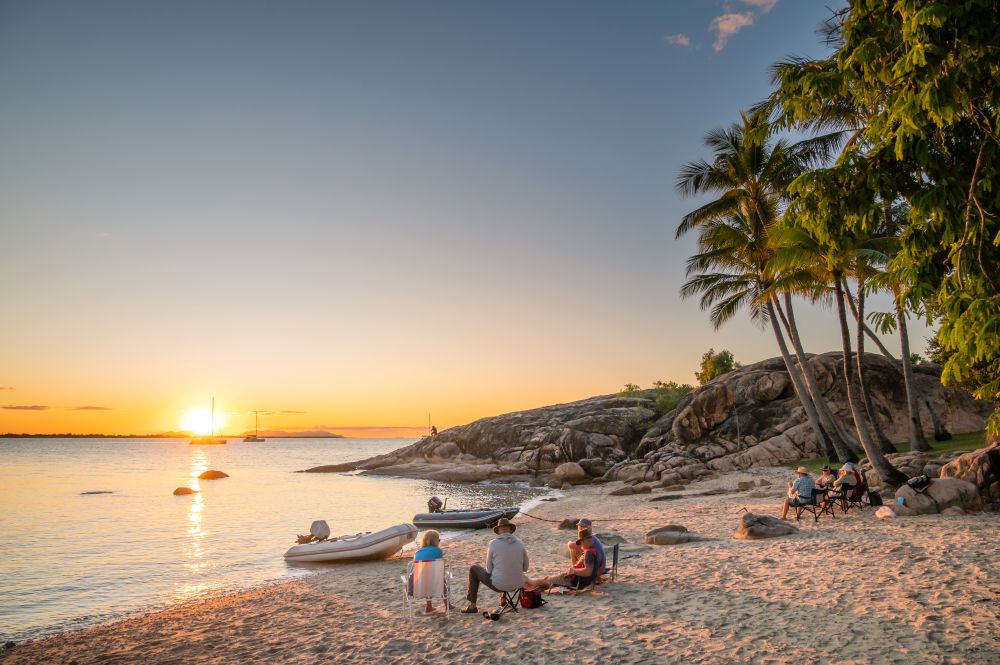 Three people sitting on Whitsunday beach admiring the golden orange sunset.